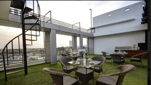 A rooftop terrace with a spiral staircase, wicker furniture, and a view of the cityscape. - Hotel Noida Dreamz 144 (Noida)