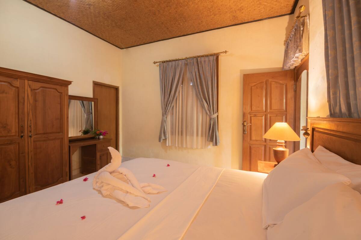 A hotel room with a bed, a nightstand with a lamp, wooden wardrobes, and a window with curtains.