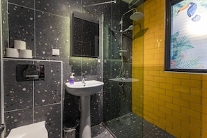 A bathroom with a black speckled tile wall, a yellow tiled accent wall, a white sink, and a glass-enclosed shower area.