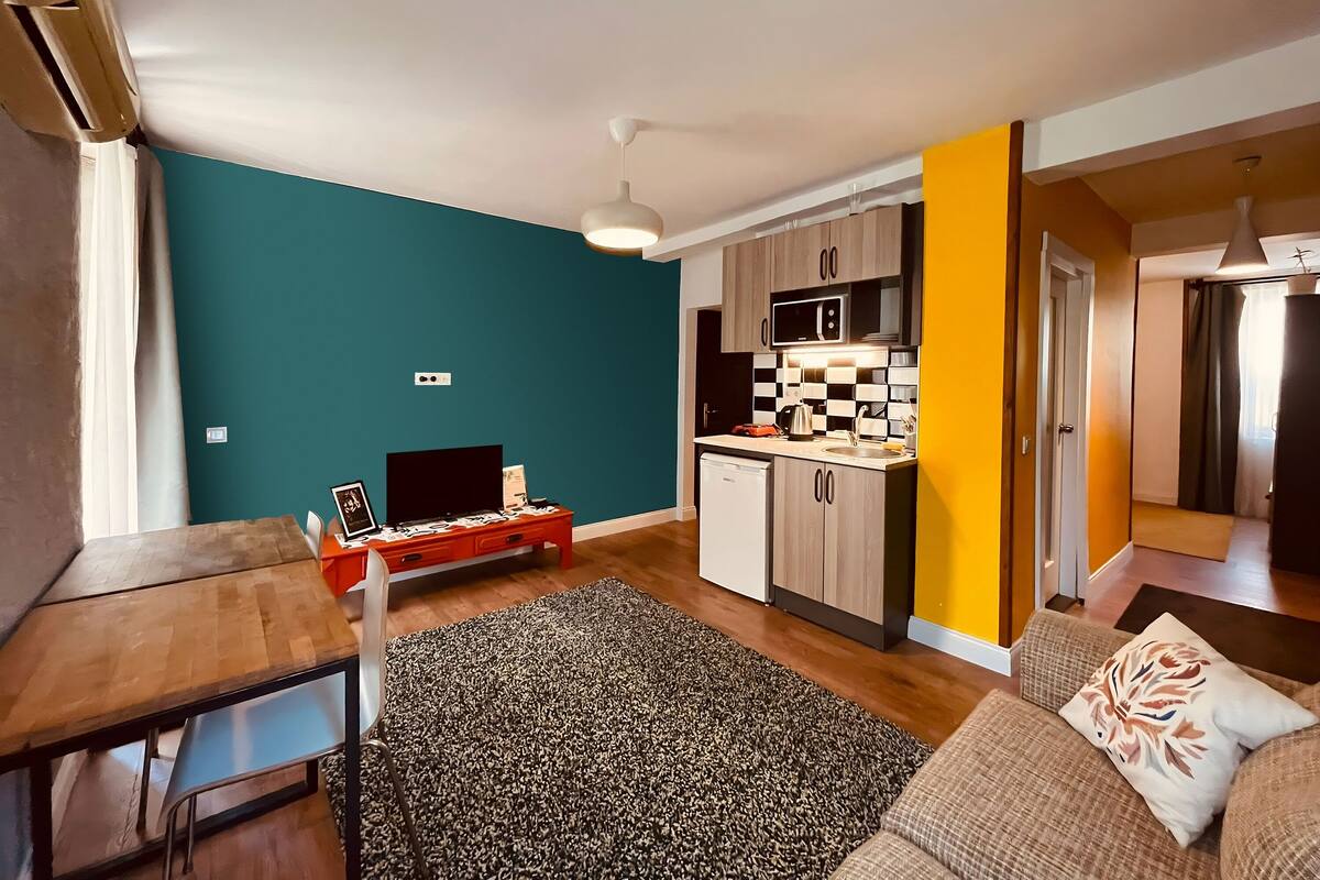 Um espaço de estar compacto com parede verde-água, cozinha com micro-ondas e área de jantar com mesa e cadeiras.