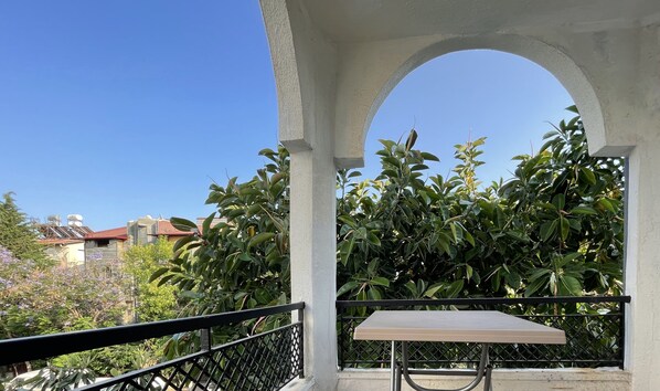 A balcony with a table and chairs, surrounded by lush green foliage and a clear blue sky.