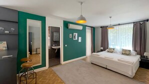 A modern bedroom with a bed, a sitting area with a stool, a bathroom with a sink, and a large mirror. - Cabbana Hotel Lara (Antalya)