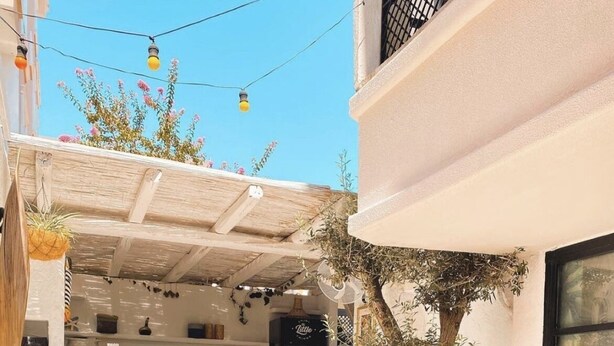 A cozy outdoor seating area with white furniture and striped cushions, a tree, and a kitchen visible in the background. - Cabbana Hotel Lara (Antalya)