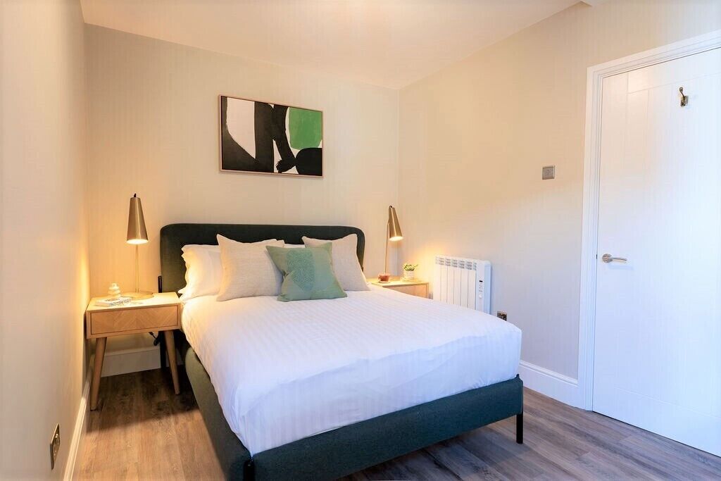 A neatly arranged bedroom with a bed, two bedside lamps, a radiator, and a door.