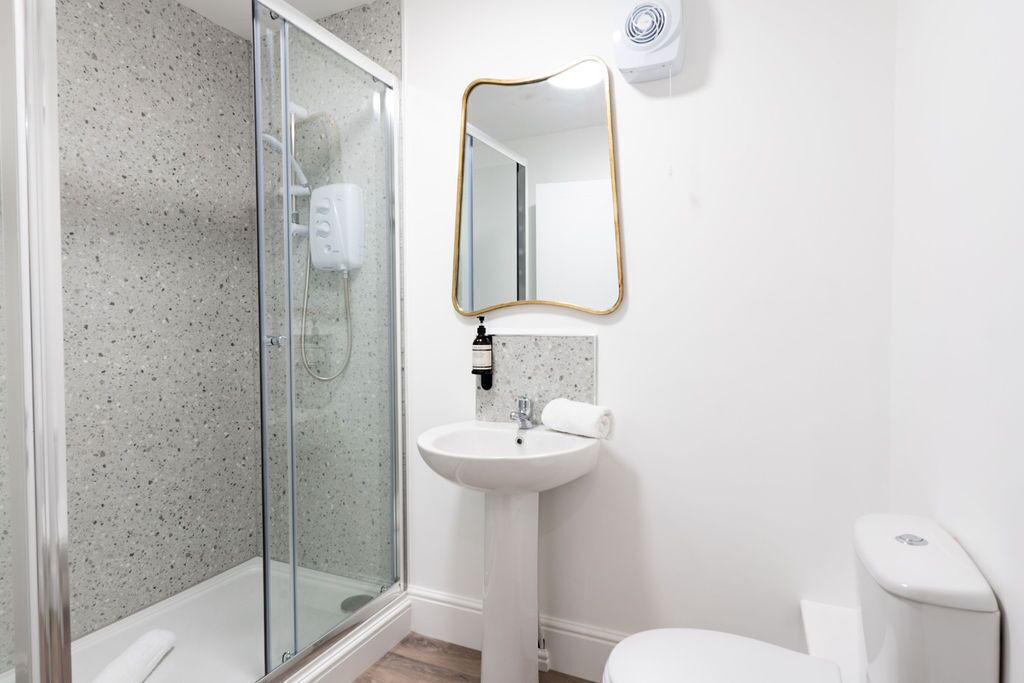 Un baño con cabina de ducha de vidrio, un lavamanos blanco, un inodoro y un espejo montado en la pared.