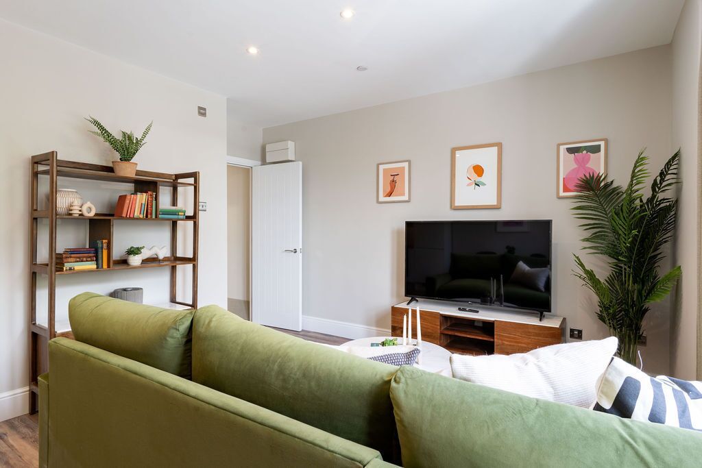 Una sala de estar moderna con un sofá verde, una estantería, un televisor de pantalla plana y obras de arte enmarcadas en la pared.