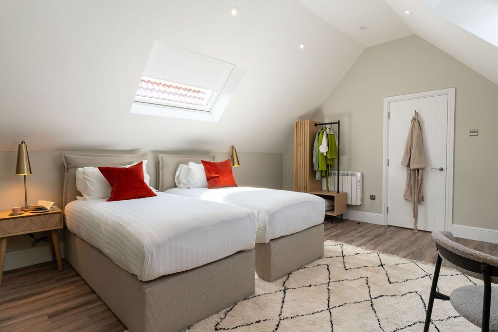 Quarto com uma cama grande, duas mesas de cabeceira, um radiador, uma porta com uma toalha pendurada e um claraboia.