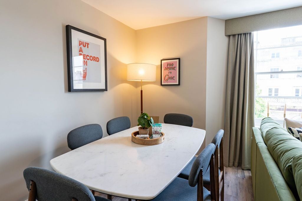 A dining area with a marble table, chairs, a lamp, and a plant. There are two framed pictures on the wall.