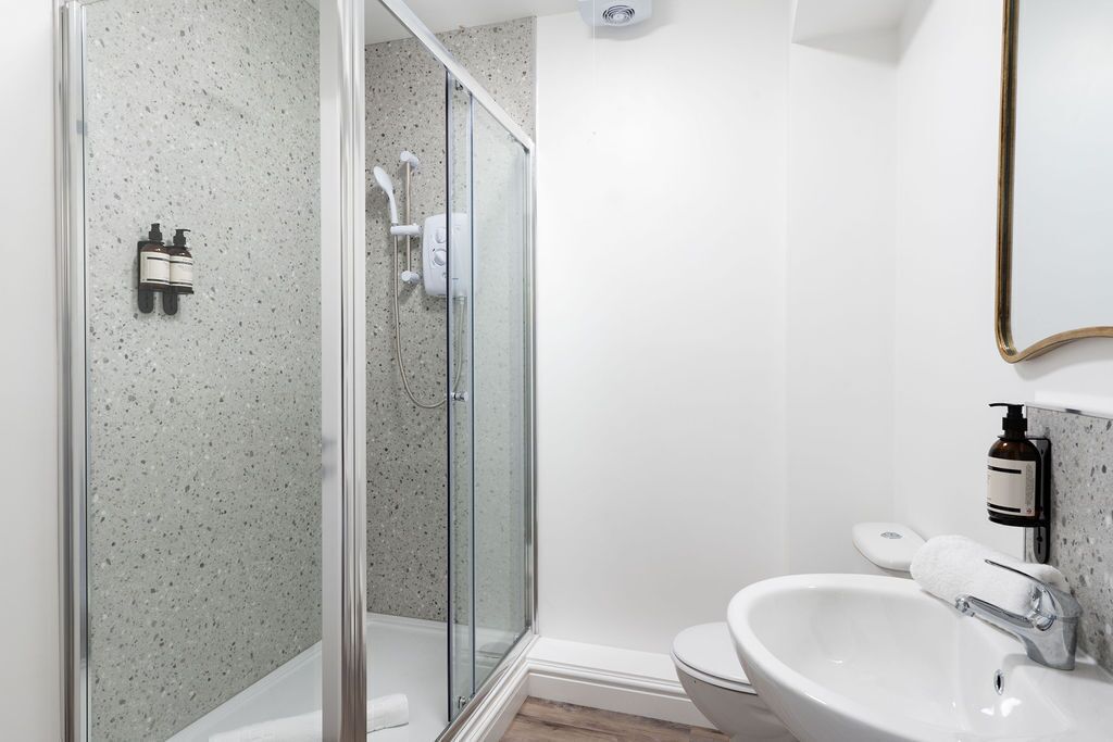 Une salle de bain moderne avec une douche à l’italienne en verre, un lavabo blanc et des toilettes.