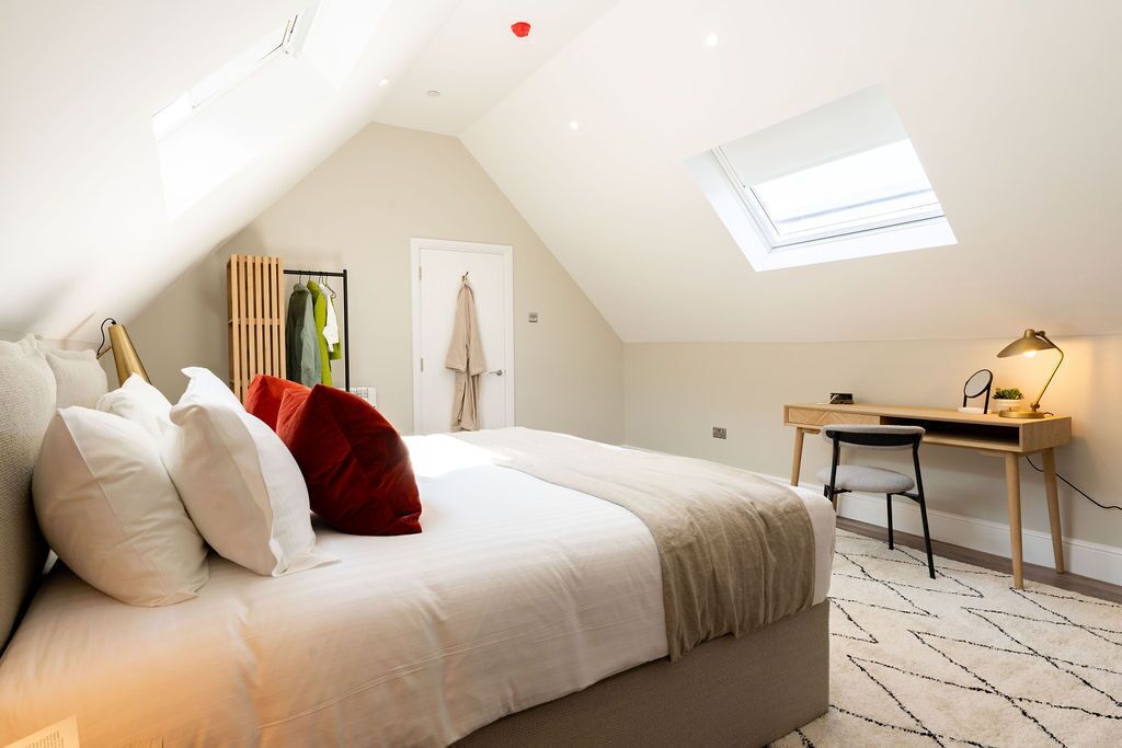A bedroom with a bed, a desk, and a skylight.