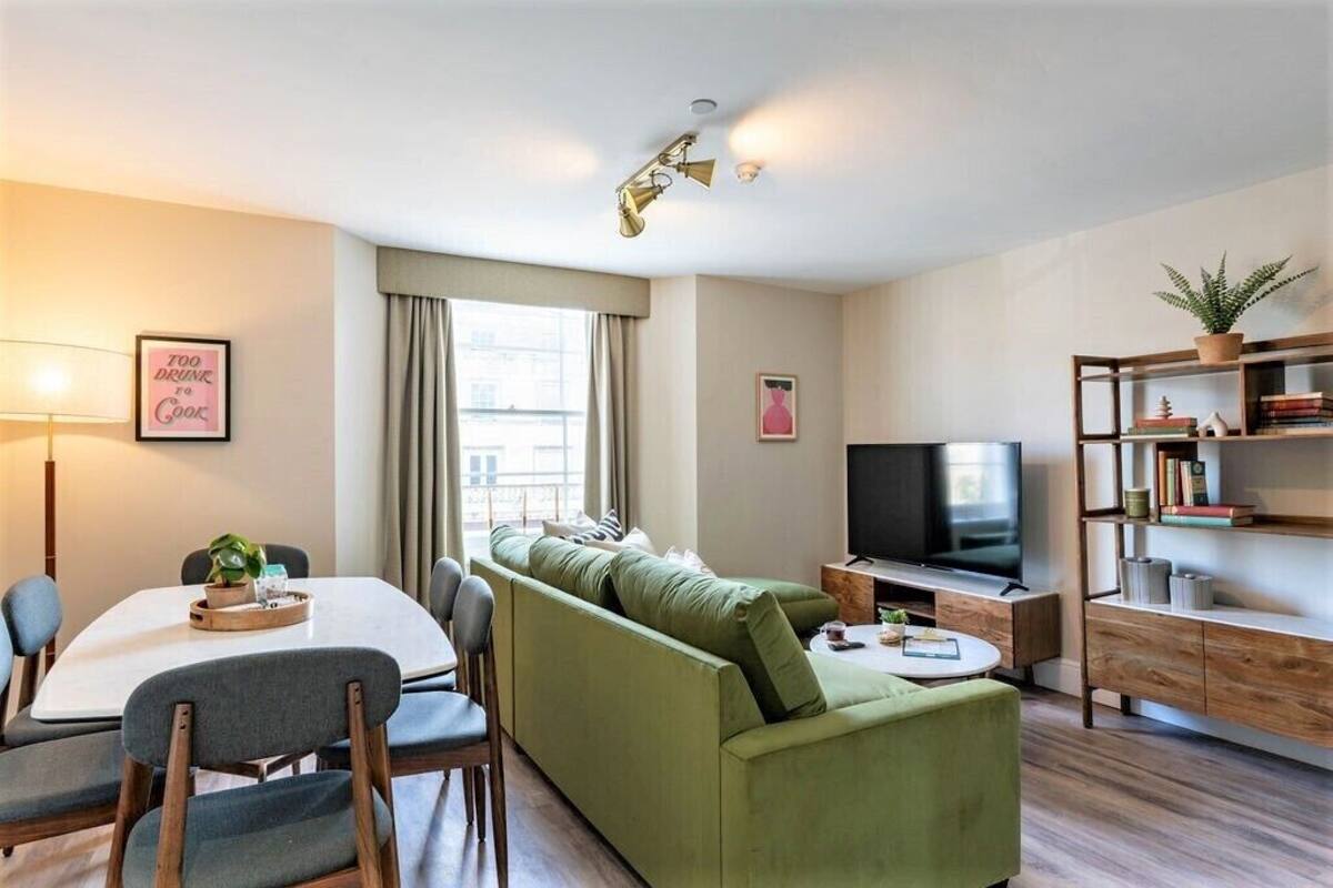 Een moderne woonkamer met een groene bank, een eettafel met stoelen, een televisie en een boekenkast.