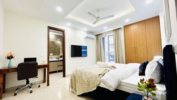Habitación de hotel con cama, escritorio, silla, televisión y una planta pequeña.