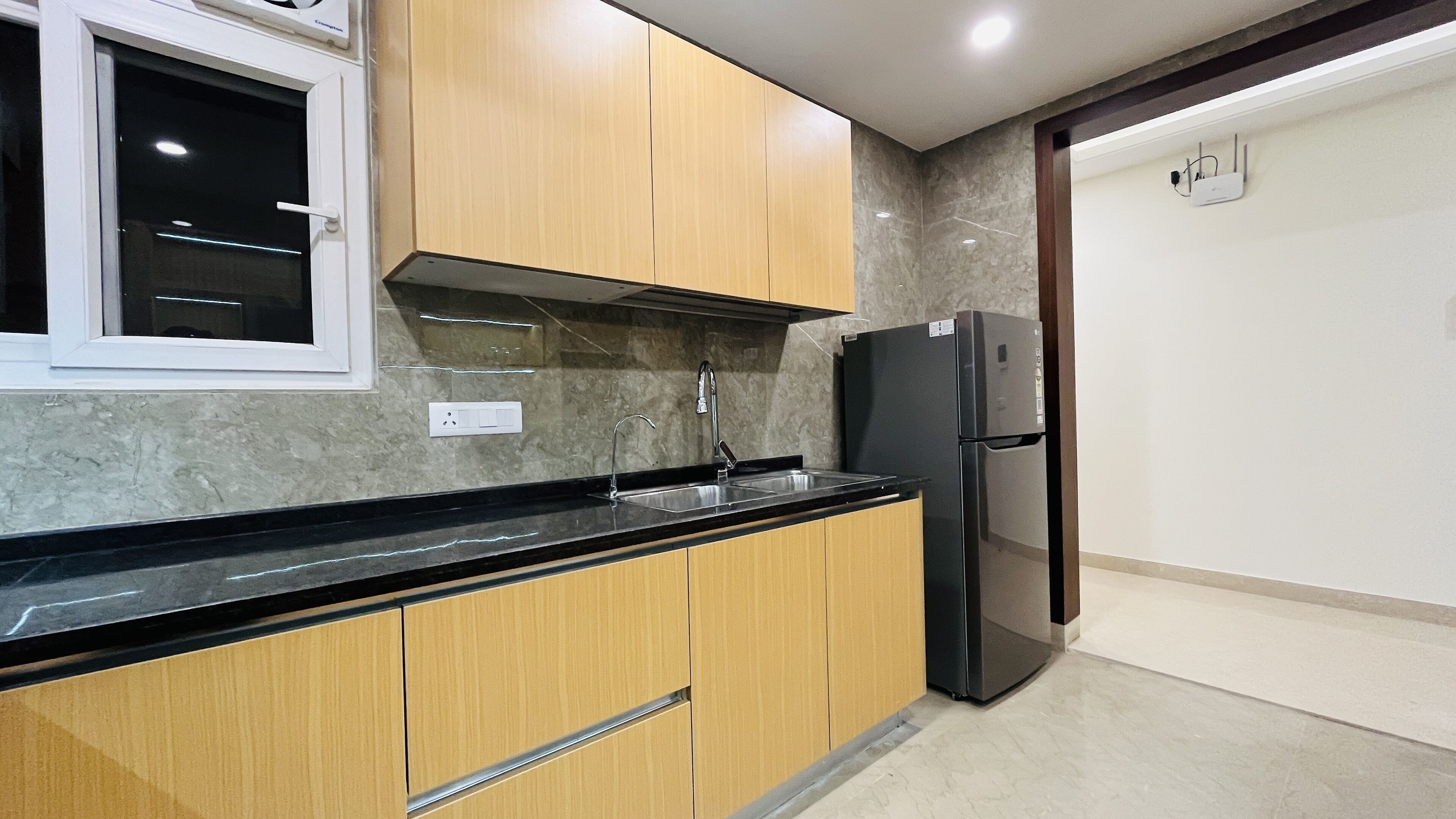 Una cocina con armarios de madera, encimera negra, pileta de acero inoxidable y refrigerador negro.