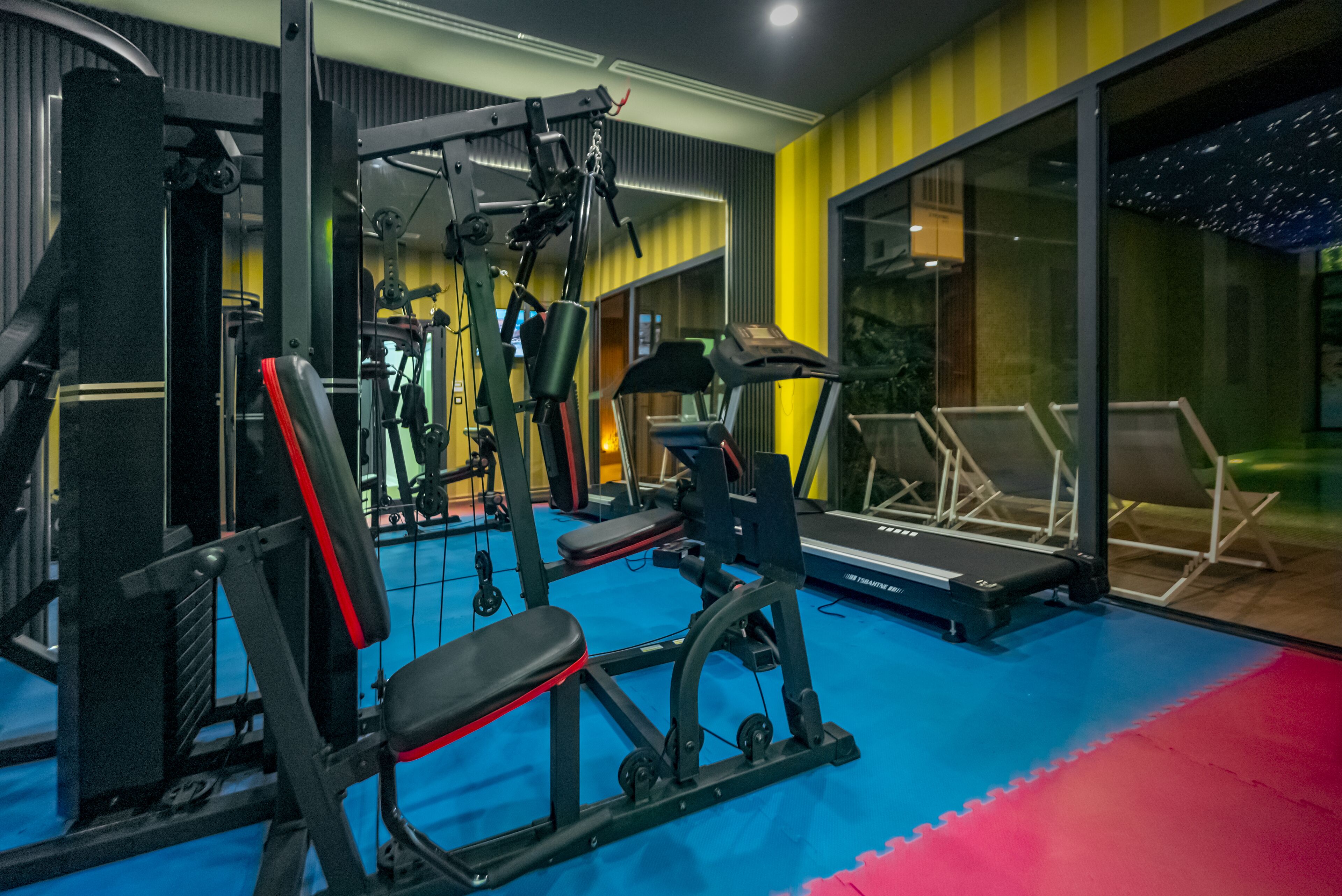 Une salle de sport équipée de matériel d’exercice, d’un tapis de course et d’un sol bleu et rouge.