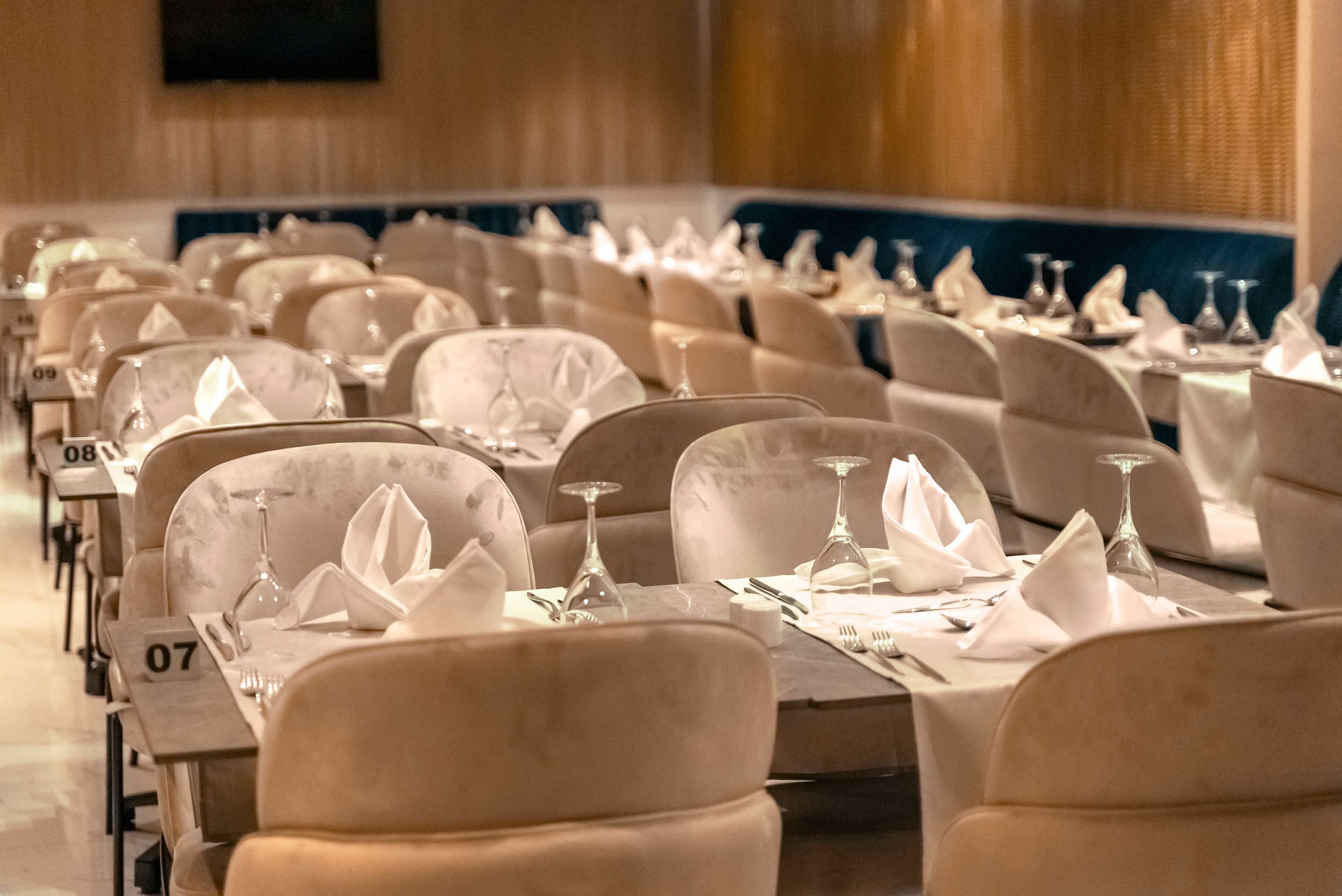 A banquet hall with rows of tables, each set with white tablecloths, napkins, and wine glasses.