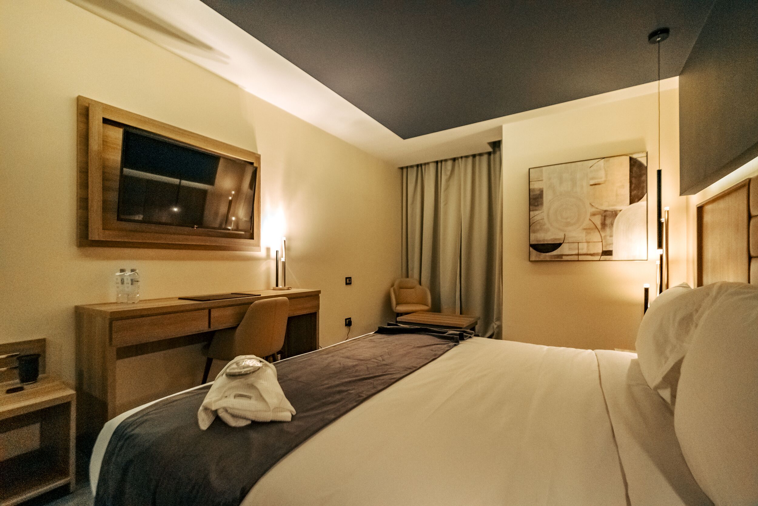 A hotel room with a bed, a desk, a chair, a mirror, and a window.