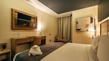 A hotel room with a bed, a desk, a chair, a mirror, and a window.
