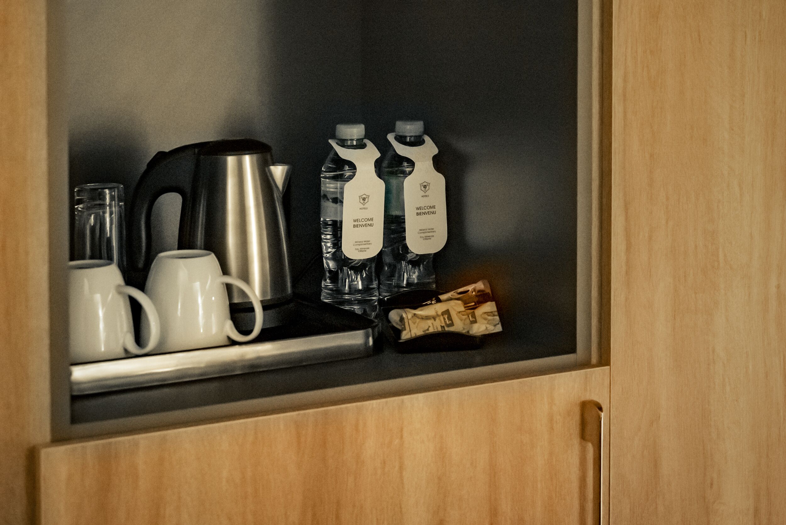 Una zona de cocina con cafetera, dos botellas de agua, una bolsita de té y un vaso.
