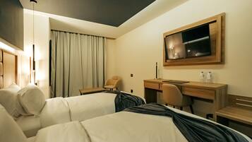 A hotel room with two beds, a desk, a chair, a TV, and a large window with curtains.