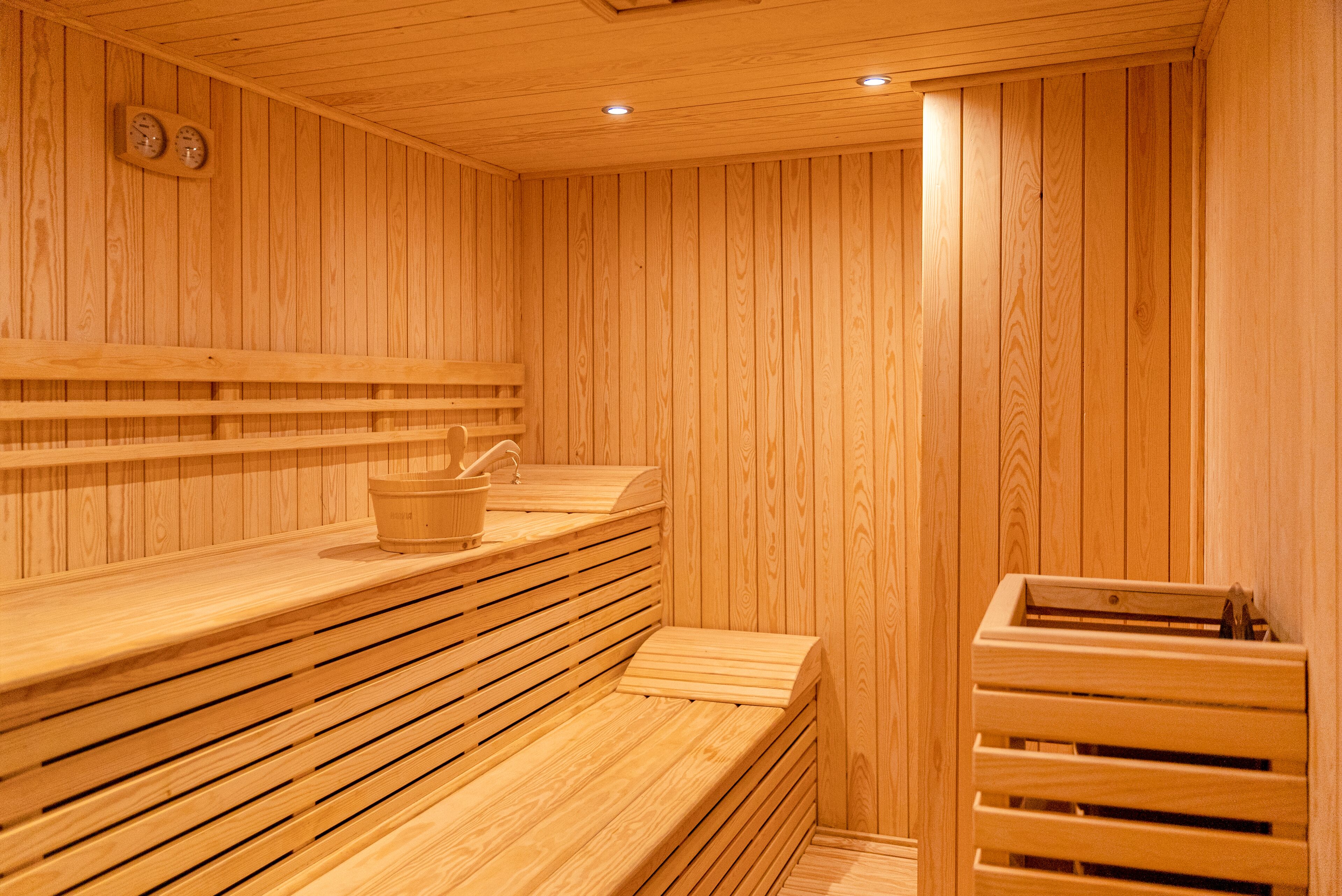 Een houten sauna met banken en een houten kist met een emmer.