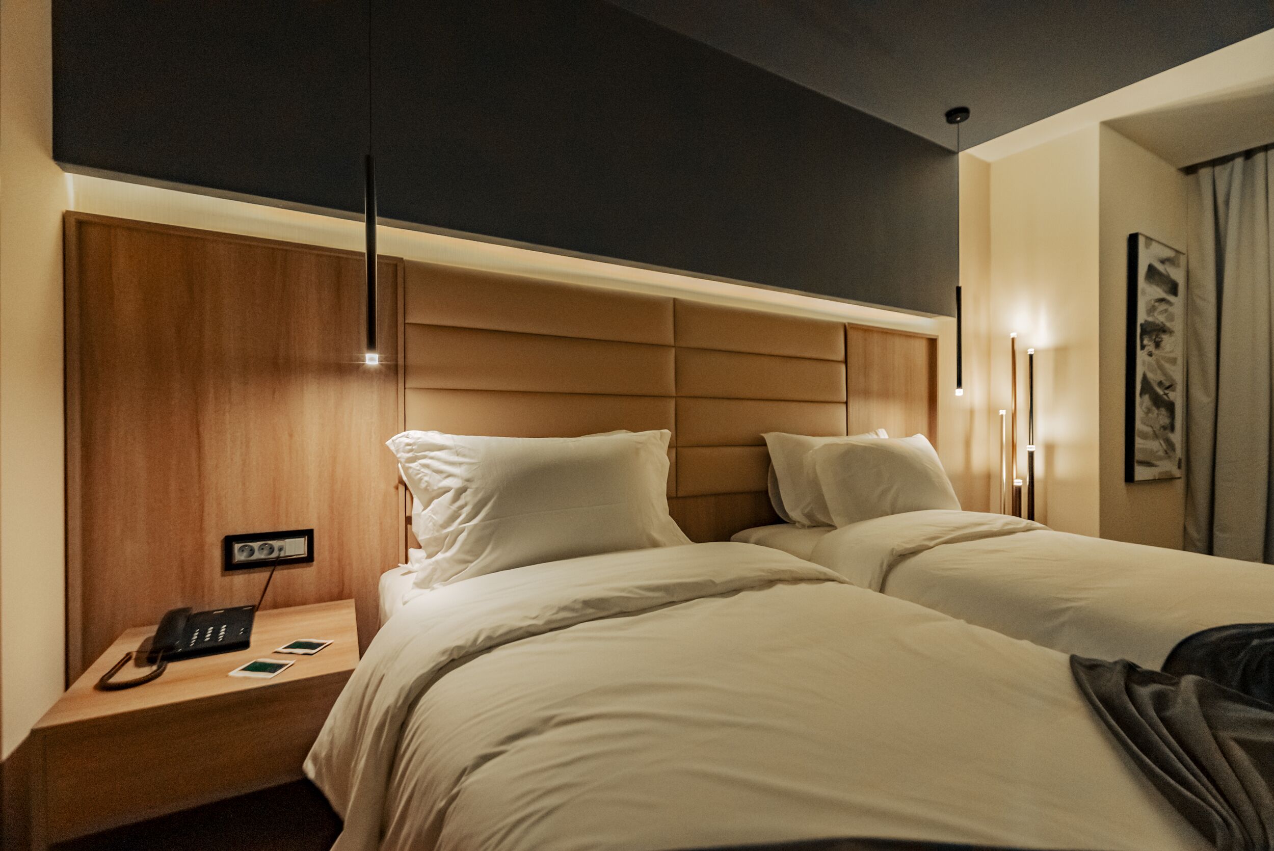 Habitación de hotel con dos camas, cabeceros de madera, mesitas de noche con lámparas y un teléfono.