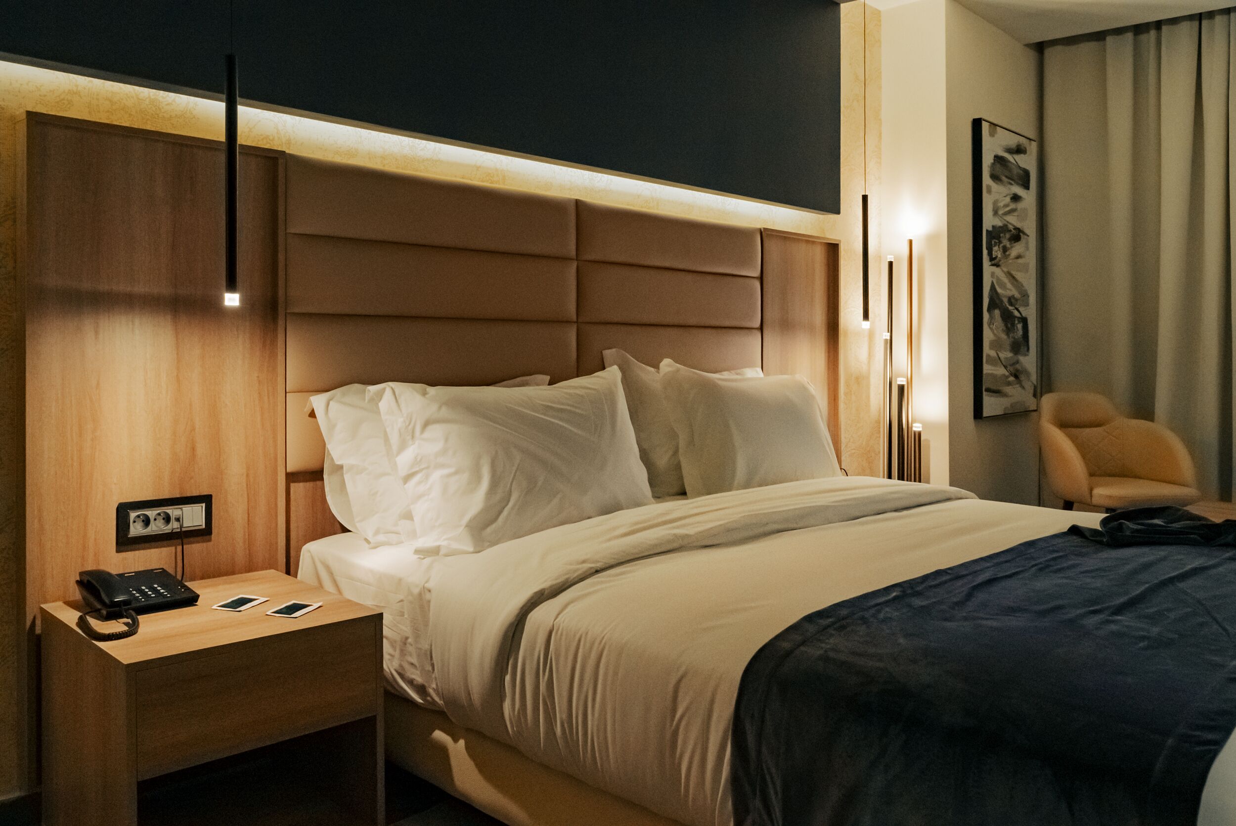 Habitación de hotel con una cama grande, una mesita de noche con teléfono, y una lámpara fijada a la pared.