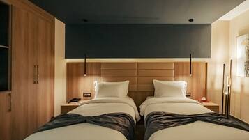 Ein Hotelzimmer mit zwei Betten, einem Holzschrank, Nachttischen mit Lampen und einem modernen Deckenstil.