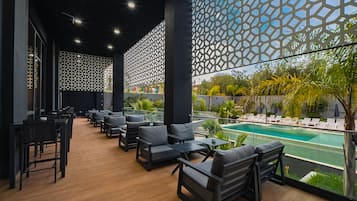 Un área de descanso al aire libre moderna con mobiliario negro, una piscina y un diseño de pared geométrico.