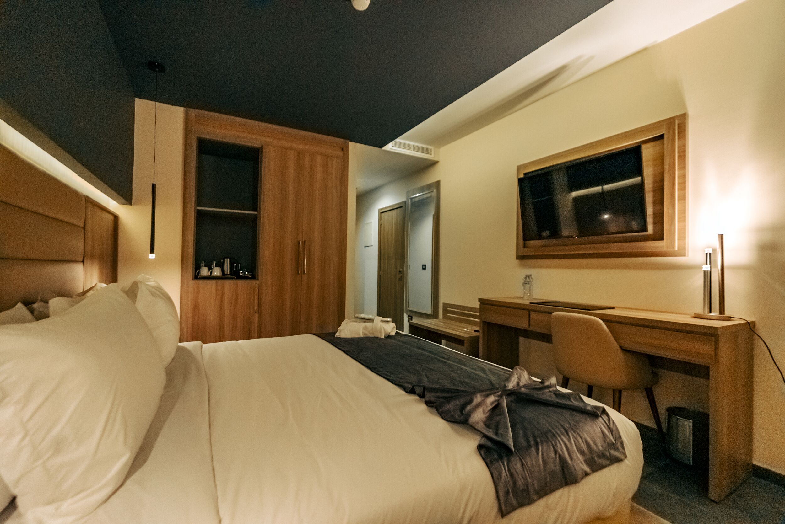 A hotel room with a bed, a desk, a chair, a wardrobe, and a mirror.