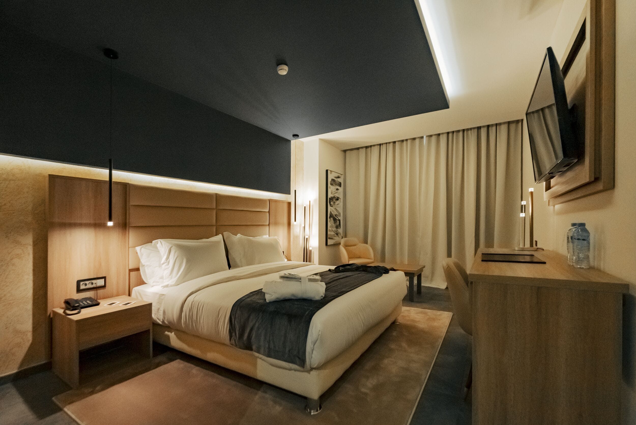 Una habitación de hotel moderna con una cama grande, mesitas de noche, un escritorio y un televisor de pantalla plana montado en la pared.
