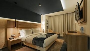 Una habitación de hotel moderna con una cama grande, mesitas de noche, un escritorio y un televisor de pantalla plana montado en la pared.