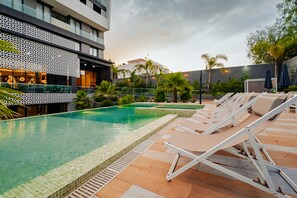A swimming pool with lounge chairs, a bar area, and a building with a patterned facade.