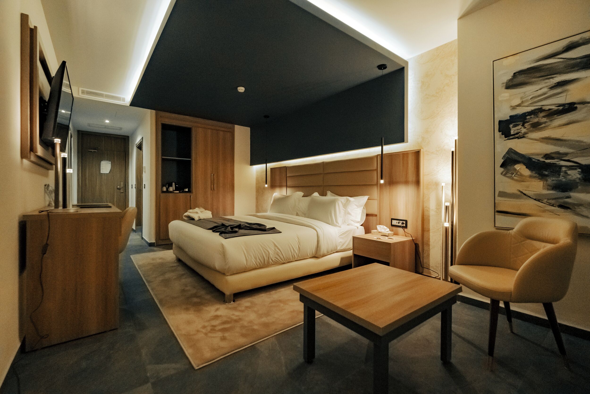 Una habitación de hotel moderna con cama, mesita de noche, silla y televisor de pantalla plana montado en la pared.
