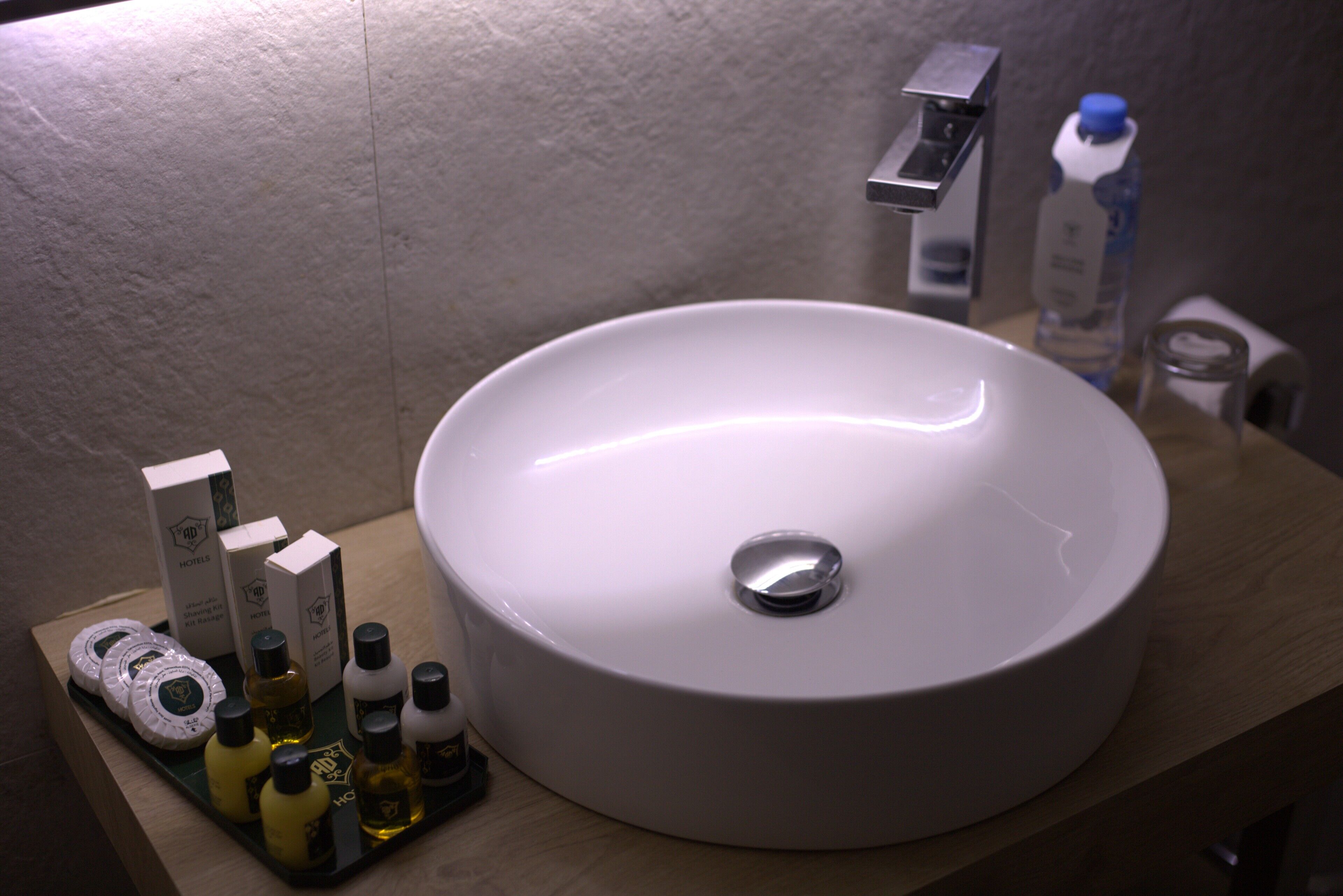 A bathroom with a round white sink, a mirror, and toiletries on a tray.
