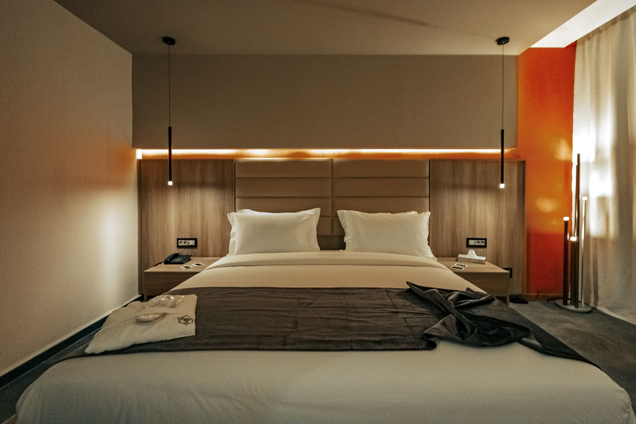 Una habitación de hotel moderna con una cama grande, dos mesitas de noche y una lámpara de pie.