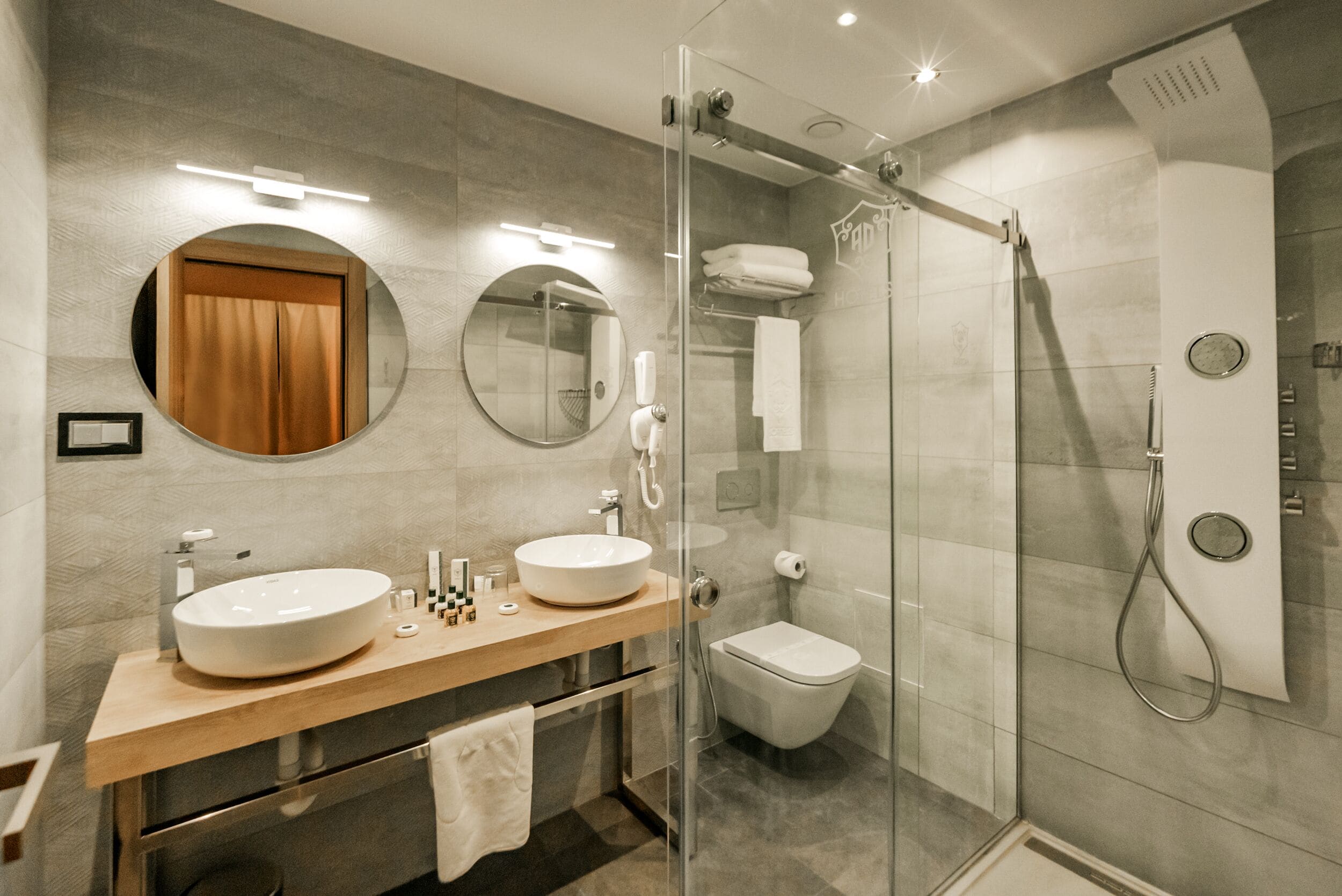 Een moderne badkamer met twee wasbakken, een toilet en een douche met glazen wanden.