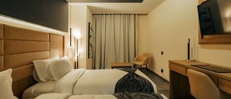 A hotel room with two beds, a desk, a chair, a TV, and a window with curtains.