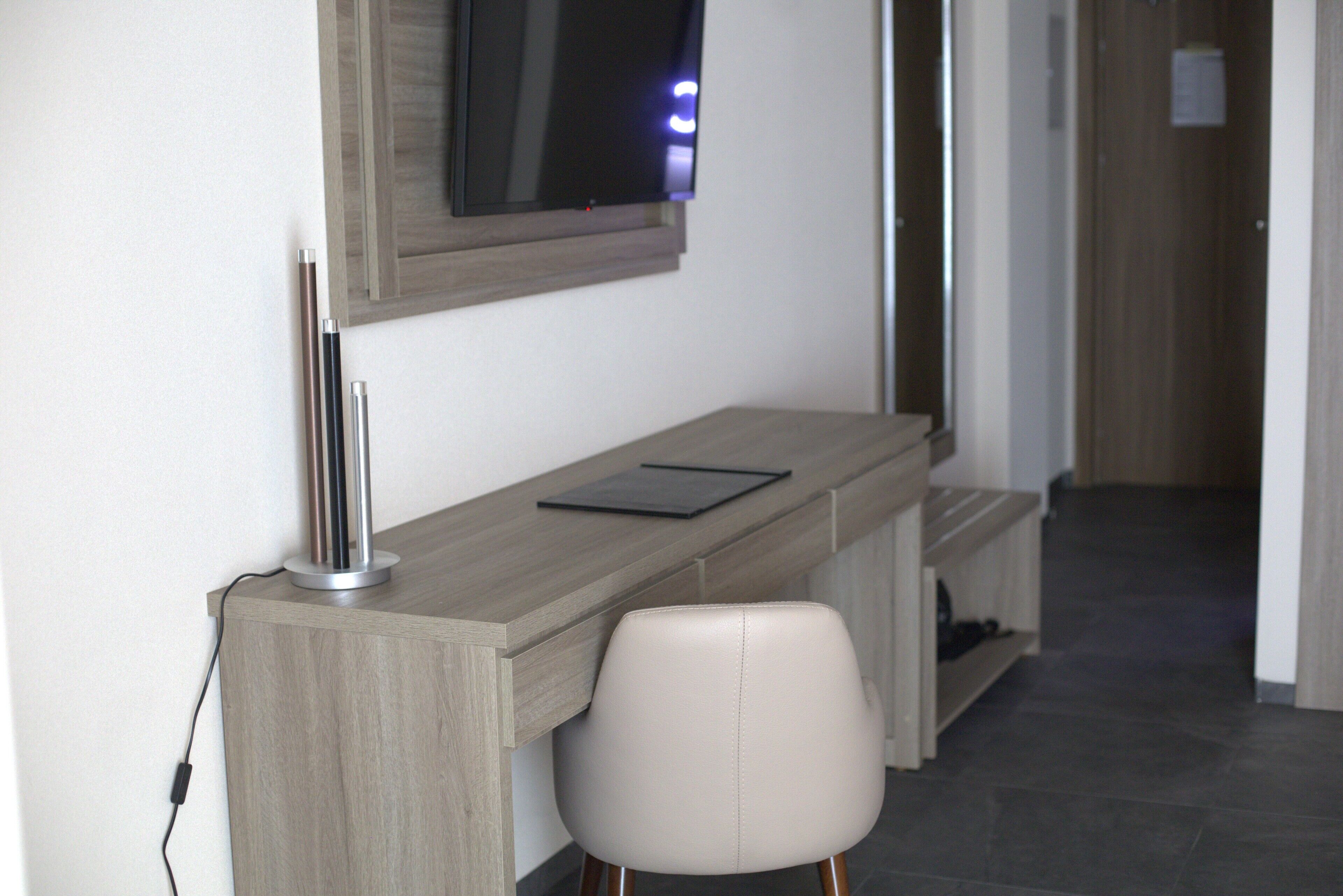 Ein moderner Arbeitsplatz mit Schreibtisch, Stuhl und Wand-Fernseher.