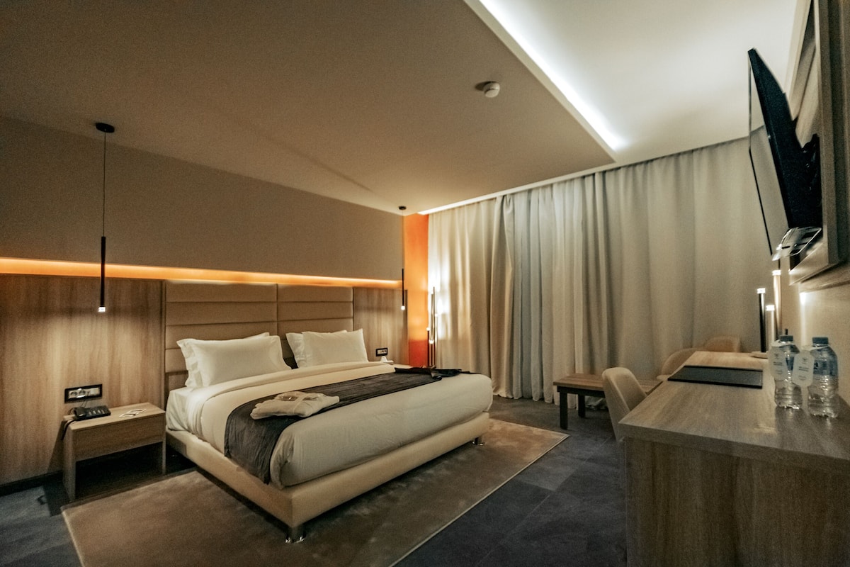 A modern hotel room with a large bed, bedside tables, a desk, and a flat-screen TV.