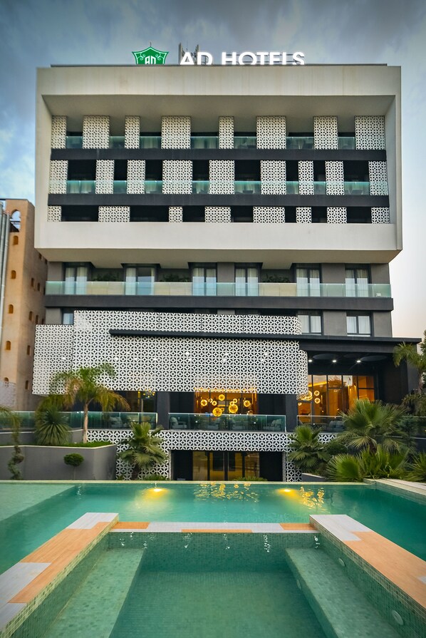 A hotel with a modern facade, multiple balconies, and a swimming pool area.
