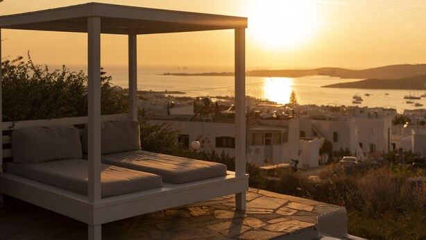 Un área de estar al aire libre iluminada por el sol con piscina, con vistas a una ciudad costera al atardecer.