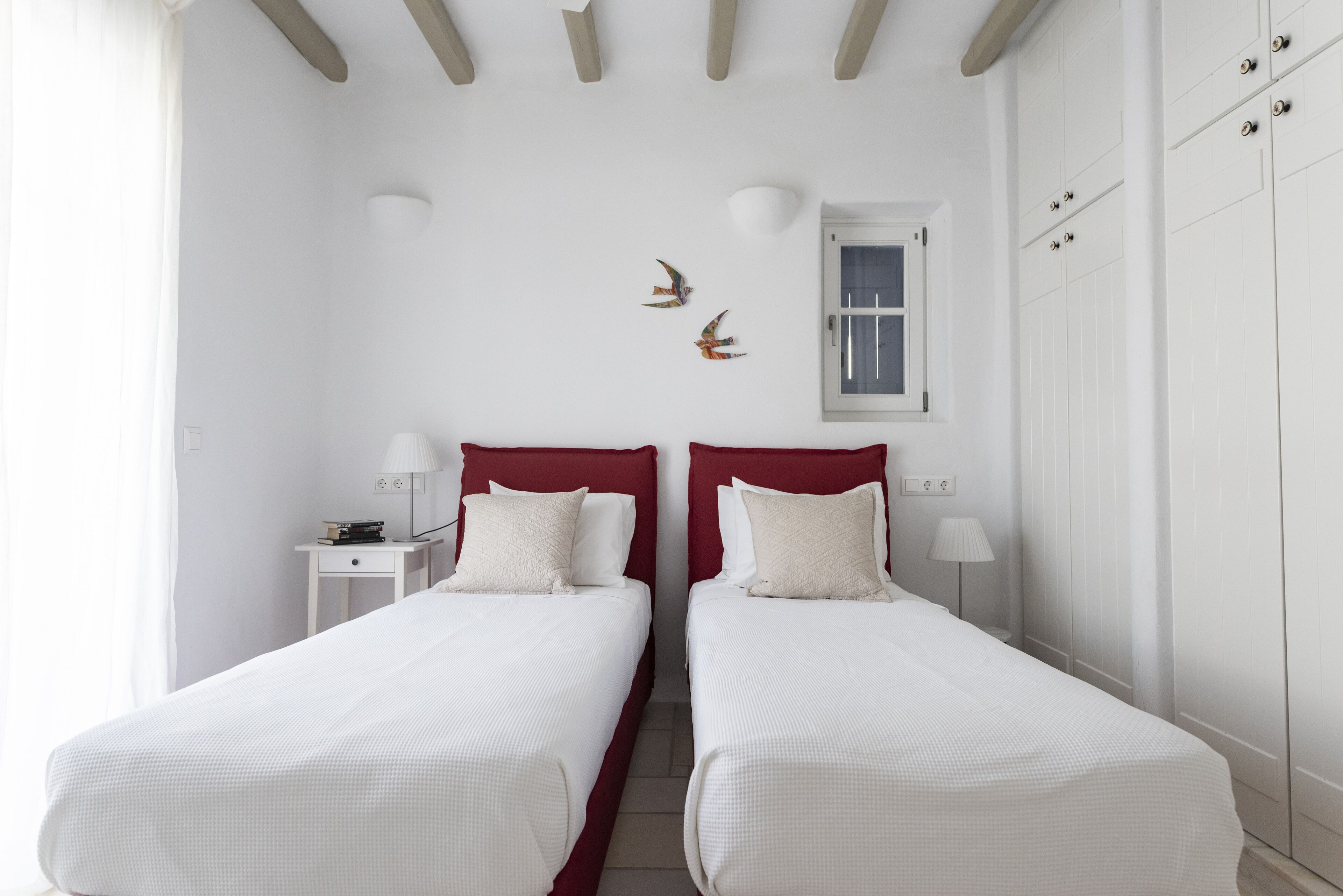A room with two single beds, white walls, a window, and a door.