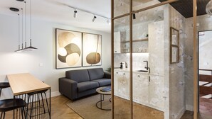 A modern living room with a sofa, a dining table, and a kitchen area visible through a glass partition. - Romántico Pied-a-terre en el Centro de Sevilla (Sevilla)