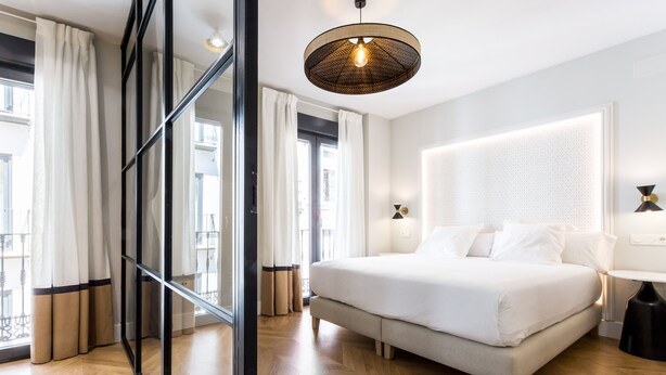 A modern hotel room with a large bed, a glass partition, and a large window with curtains. - Romántico Pied-a-terre en el Centro de Sevilla (Sevilla)