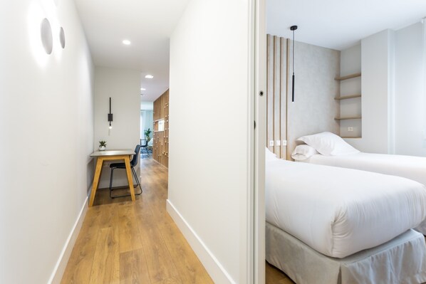 Et moderne hotelværelse med trægulv, et skrivebord med stol, en seng og et lille bord med en plante.