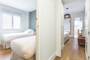 Et hotelværelse med to senge, trægulv, et stort vindue og et badeværelse med spejl og håndklædestang.