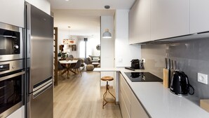 A modern kitchen with stainless steel appliances, a wooden stool, and a coffee maker. - Spacious and luxurious designer apartment in the heart of Seville (Sevilla)