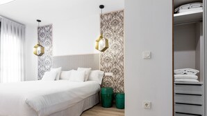 A modern hotel room with a large bed, two green trash bins, a closet with folded towels, and patterned wallpaper. - Spacious and luxurious designer apartment in the heart of Seville (Sevilla)