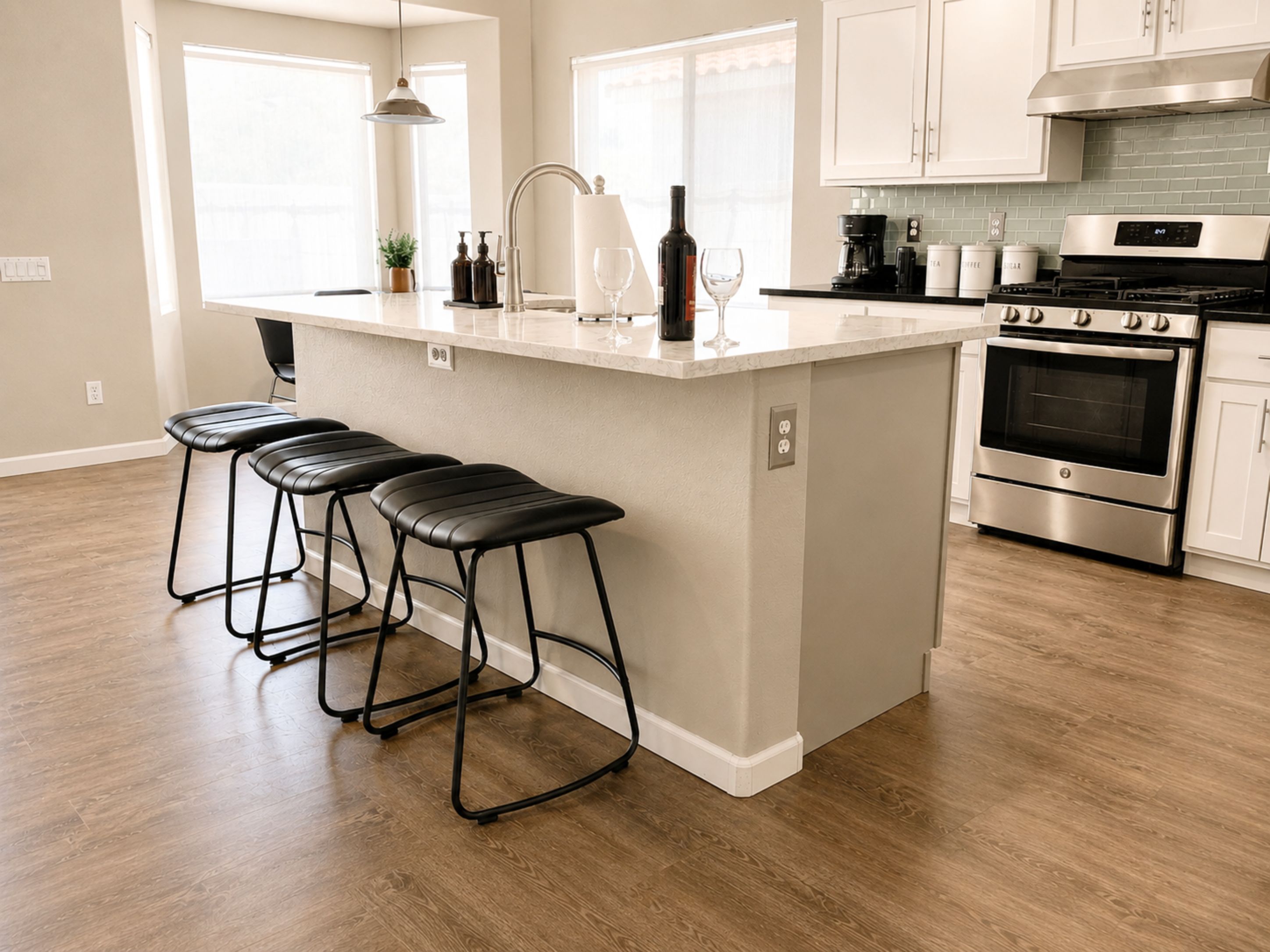 A kitchen with a central island, bar stools, stainless steel appliances, and a view of the outdoors.
