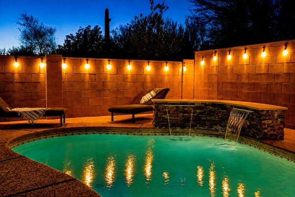 A swimming pool with a waterfall feature, surrounded by brick walls and string lights.